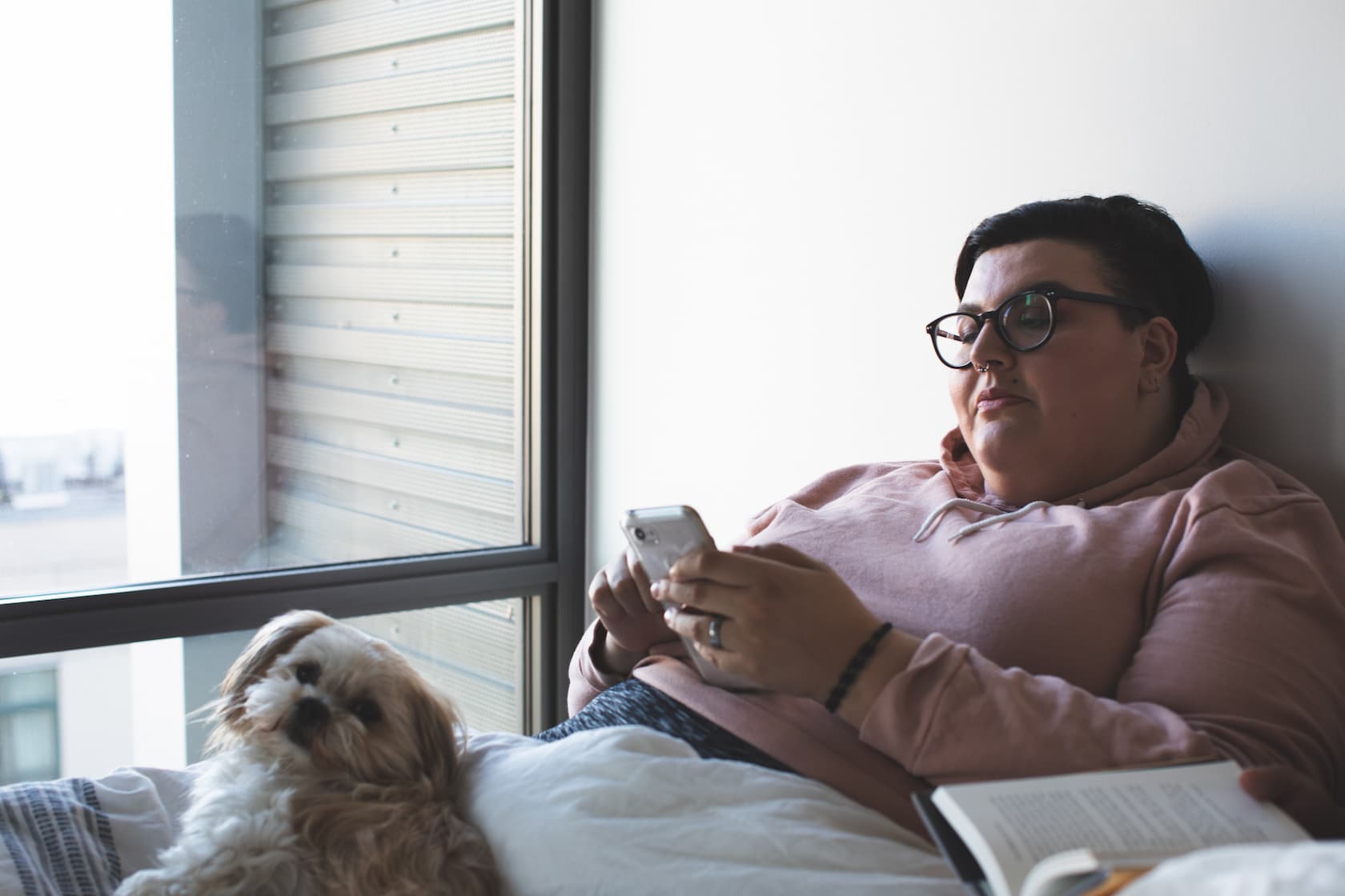 Woman looking at phone on bed with dog